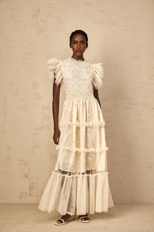 A cream white maxi dress with floral embroidery and tiered tulle skirt worn by a woman