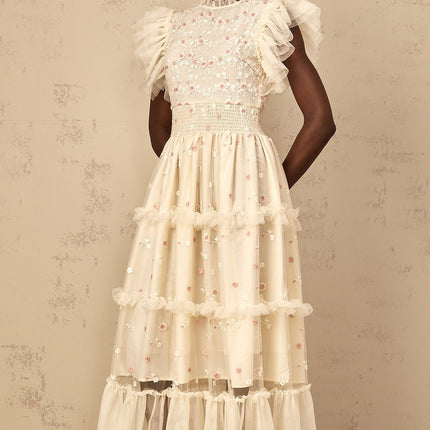A cream white maxi dress with floral embroidery and tiered tulle skirt worn by a woman