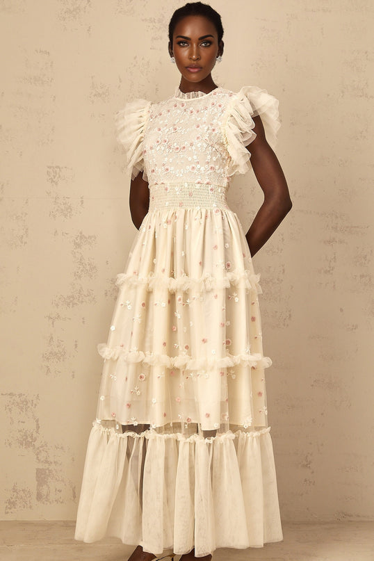 A cream white maxi dress with floral embroidery and tiered tulle skirt worn by a woman