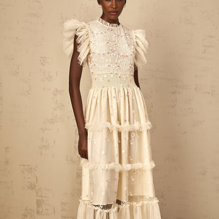 A cream white maxi dress with floral embroidery and tiered tulle skirt worn by a woman