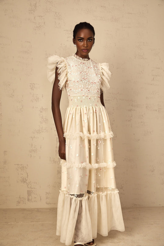 A cream white maxi dress with floral embroidery and tiered tulle skirt worn by a woman
