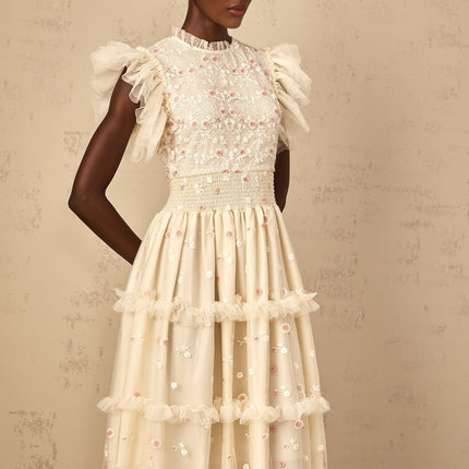 A cream white maxi dress with floral embroidery and tiered tulle skirt worn by a woman