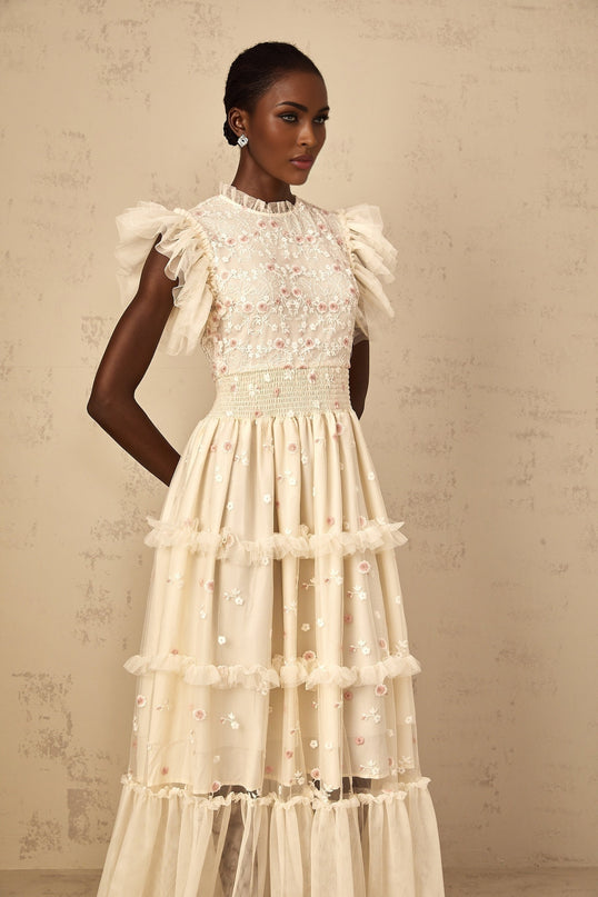 A cream white maxi dress with floral embroidery and tiered tulle skirt worn by a woman