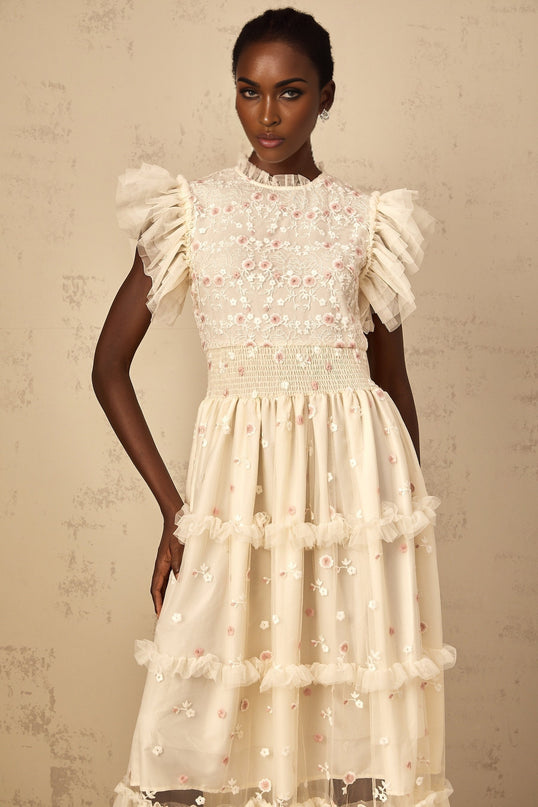 A cream white maxi dress with floral embroidery and tiered tulle skirt worn by a woman