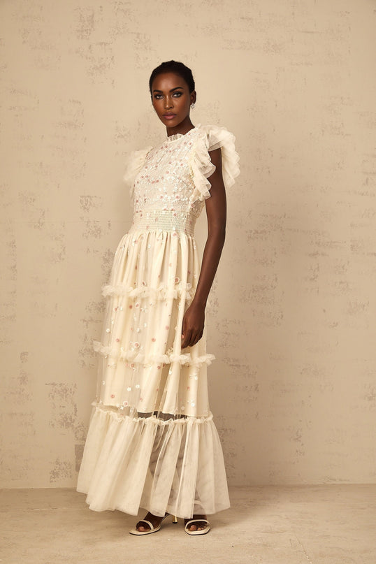 A cream white maxi dress with floral embroidery and tiered tulle skirt worn by a woman