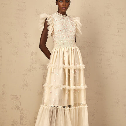 A cream white maxi dress with floral embroidery and tiered tulle skirt worn by a woman