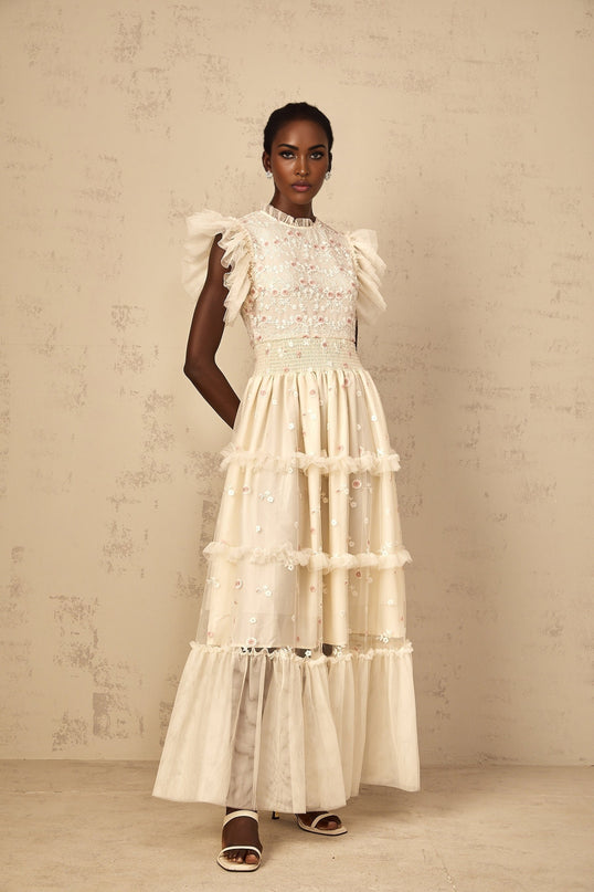 A cream white maxi dress with floral embroidery and tiered tulle skirt worn by a woman