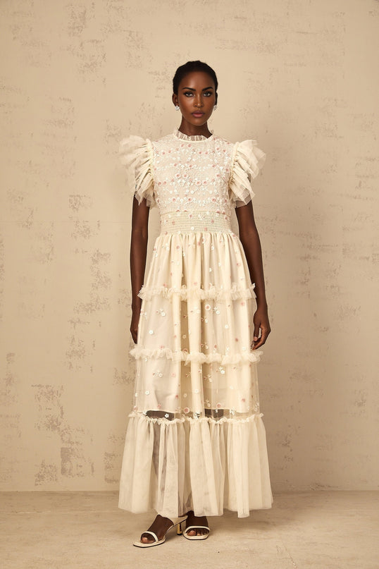 A cream white maxi dress with floral embroidery and tiered tulle skirt worn by a woman