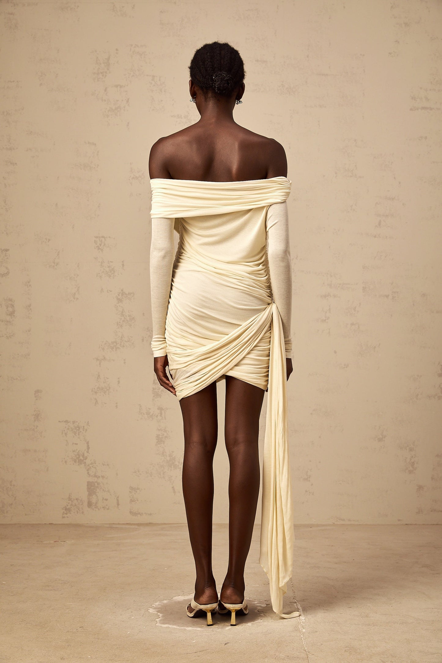 A creamwhite mini dress with ruched fabric featuring a ribbon design named Margaux The dress has a short length and likely a fitted silhouette with gathered details throughout