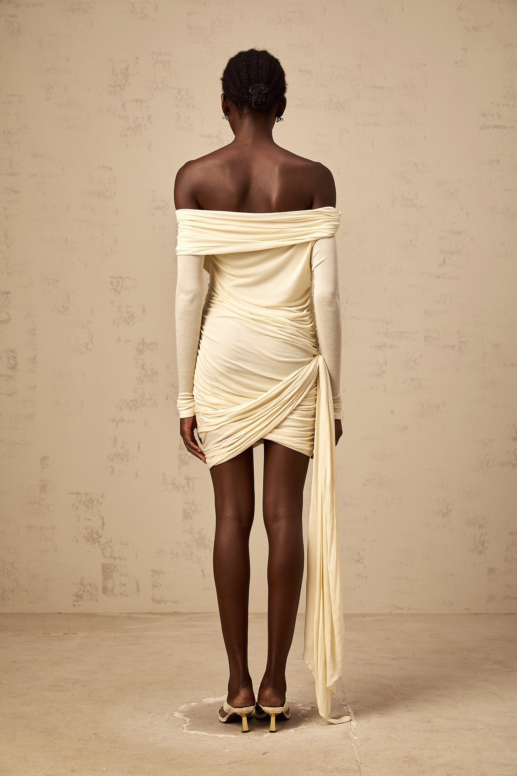 A creamwhite mini dress with ruched fabric featuring a ribbon design named Margaux The dress has a short length and likely a fitted silhouette with gathered details throughout