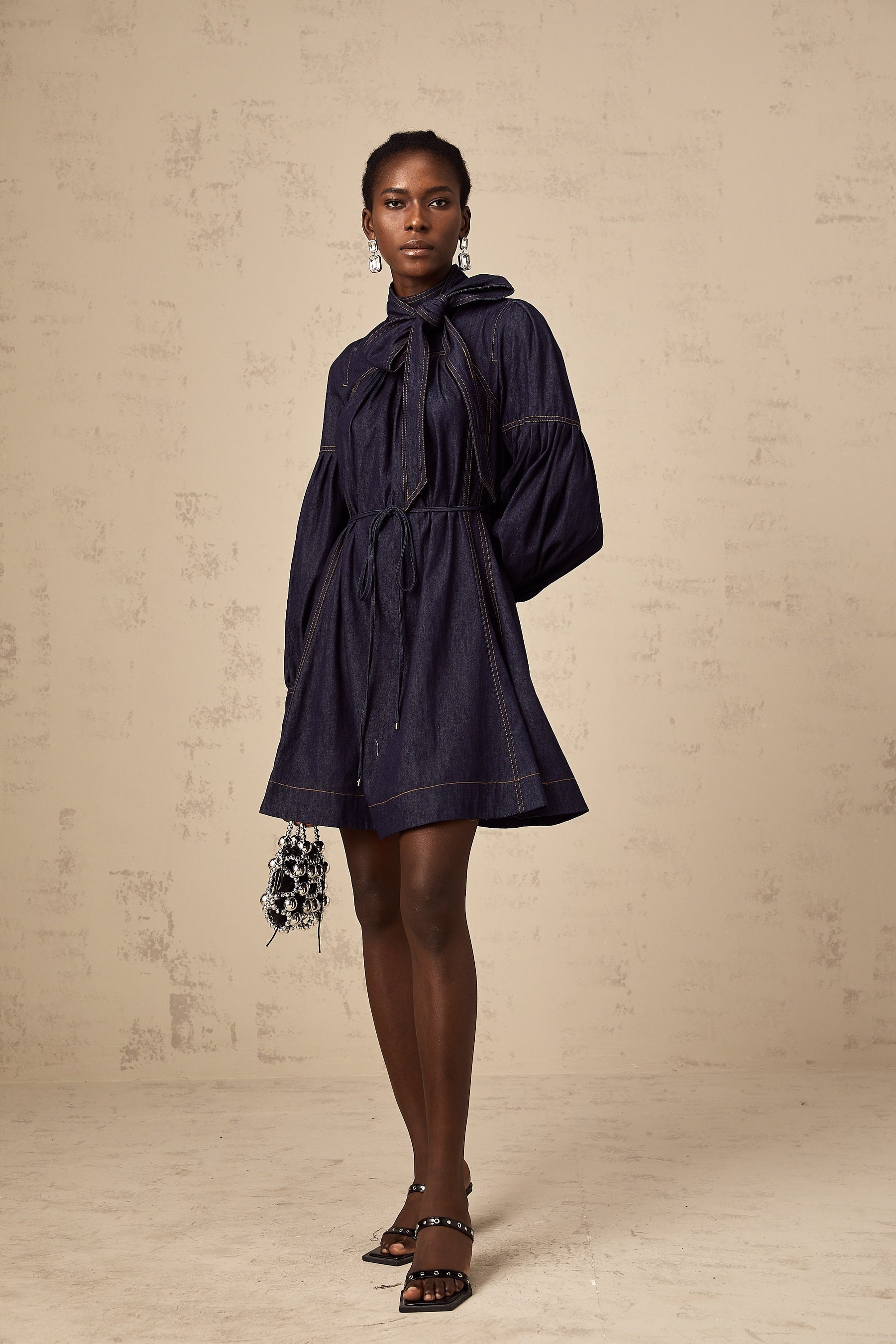 A dark blue denim mini dress with visible contrast stitching featuring a fitted silhouette and short length