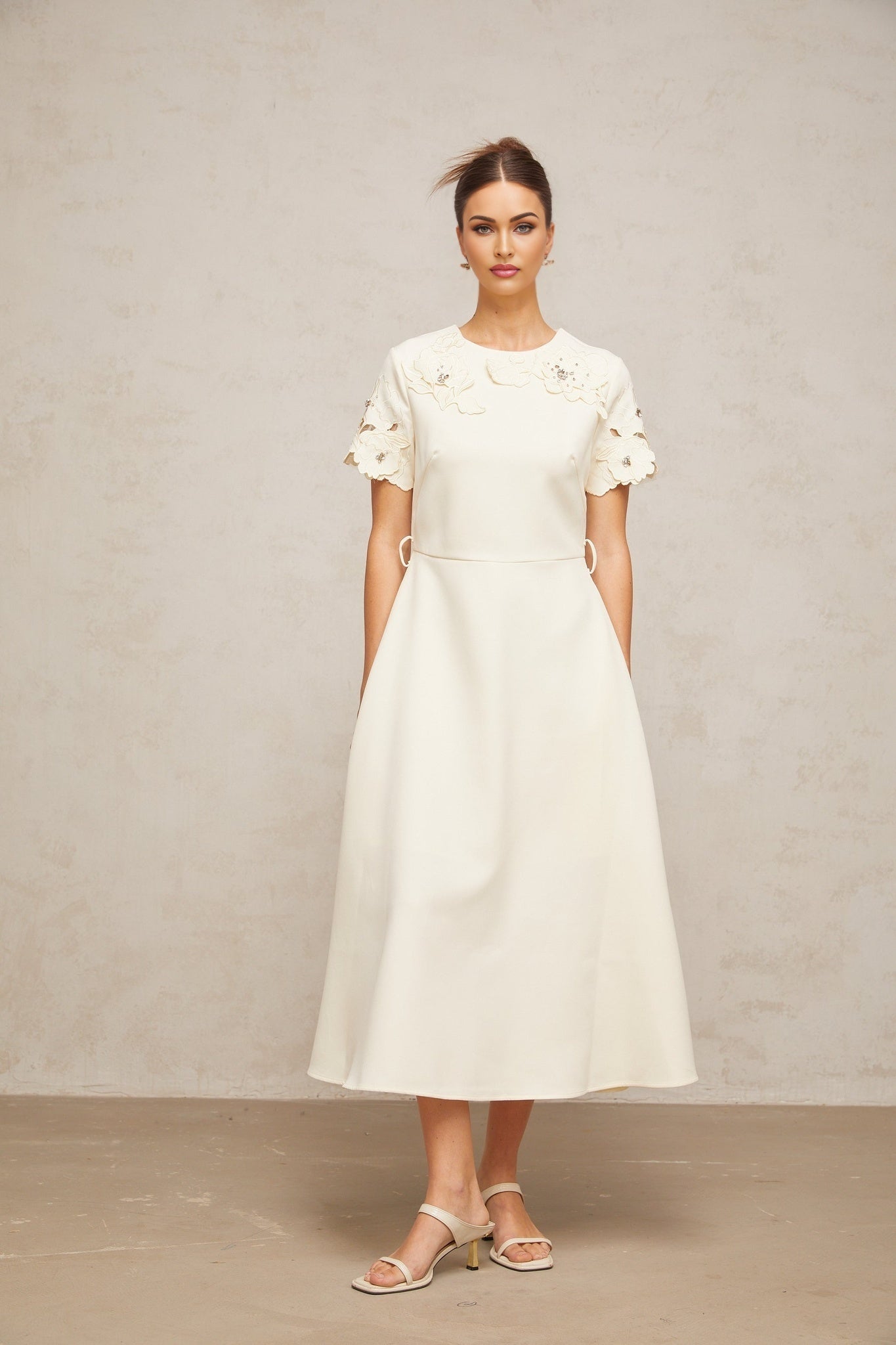 A flared midi dress in neutral tones featuring floral appliqué details and an orane color accent