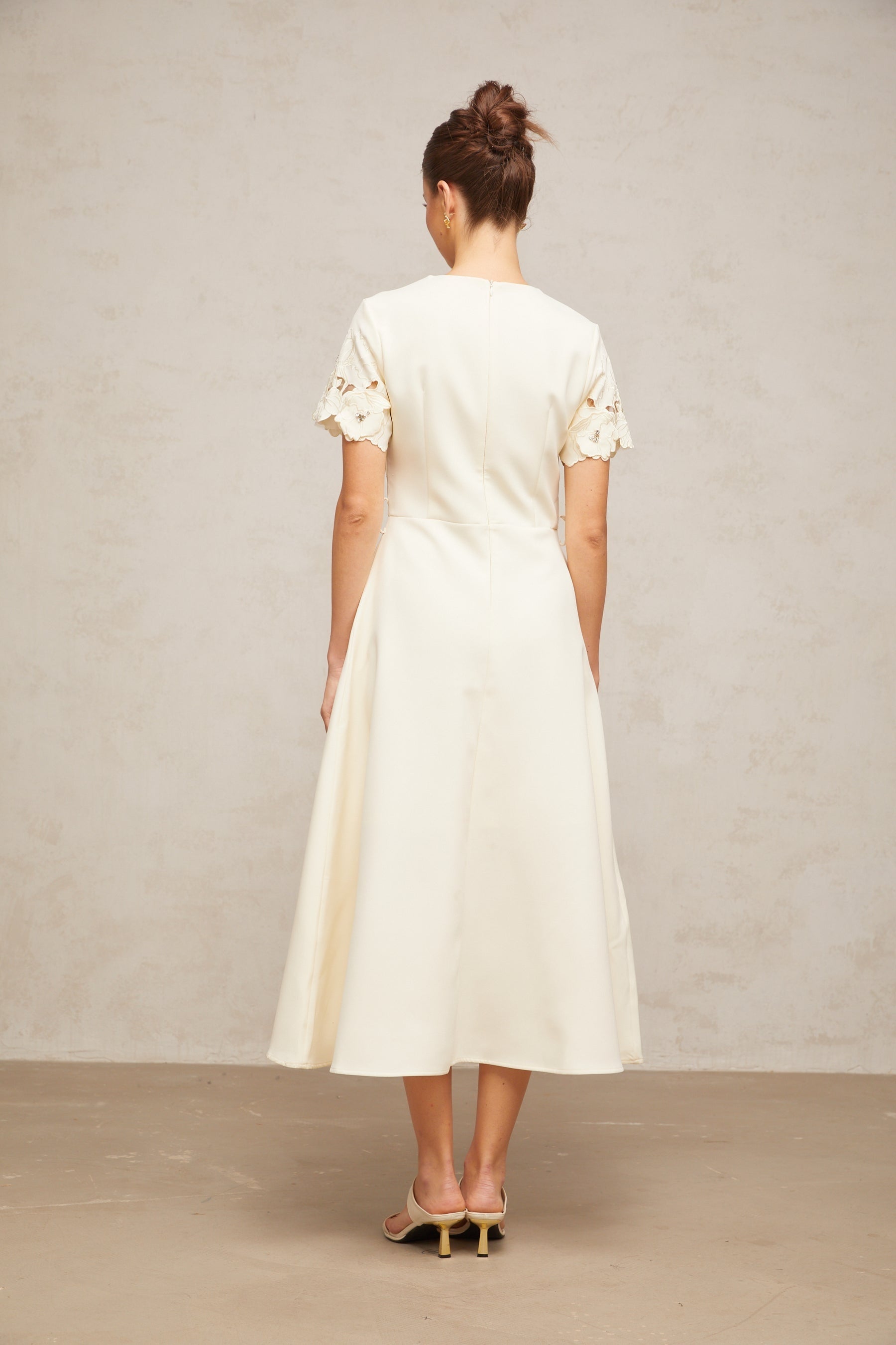 A flared midi dress in neutral tones featuring orange floral appliqués with a fitted bodice and flowing skirt