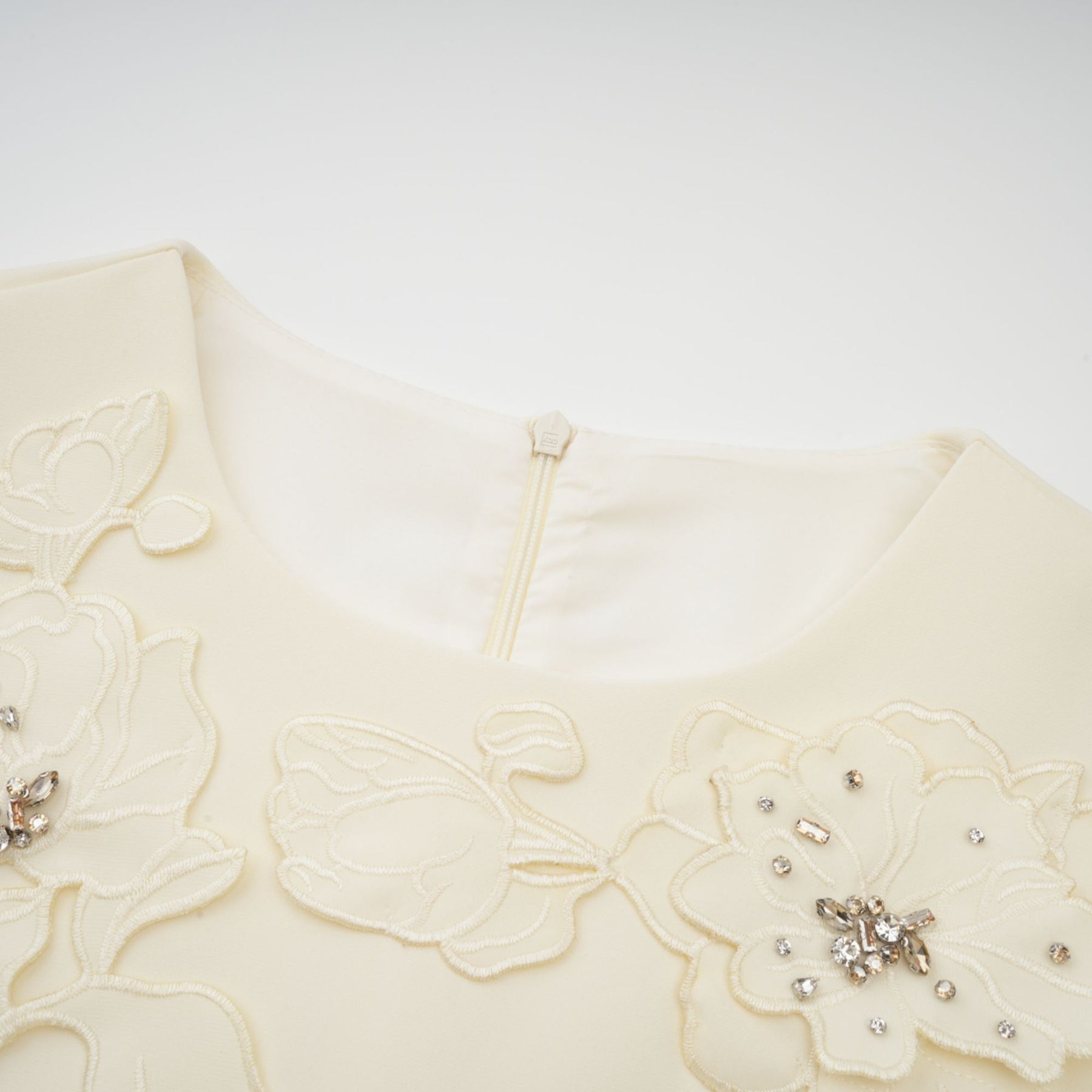 A flared midi dress in neutral tones featuring orange floral appliqués with a fitted bodice and flowing skirt