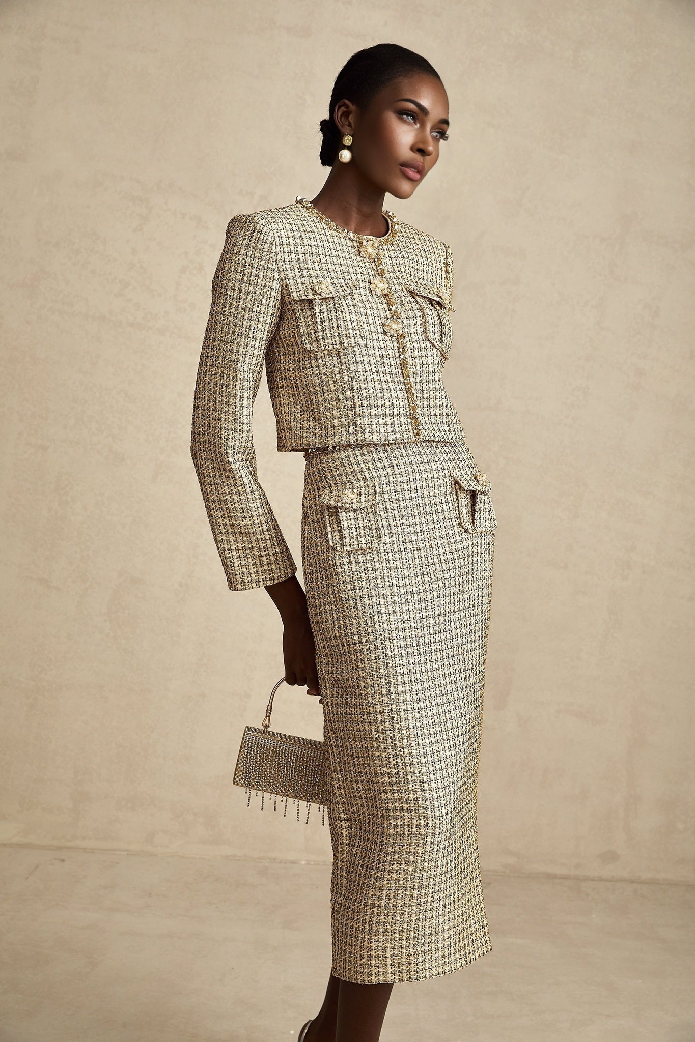 A gold colored tweed jacket and matching skirt set with sequin embellishments The outfit has a luxurious and festive appearance suitable for formal occasions