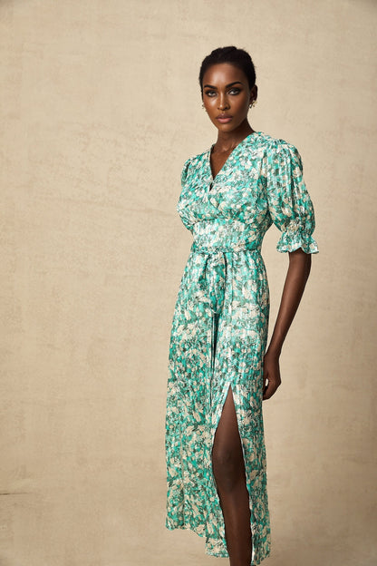 A green midi dress with a floral print pattern and a high slit featuring a feminine silhouette and flowing fabric