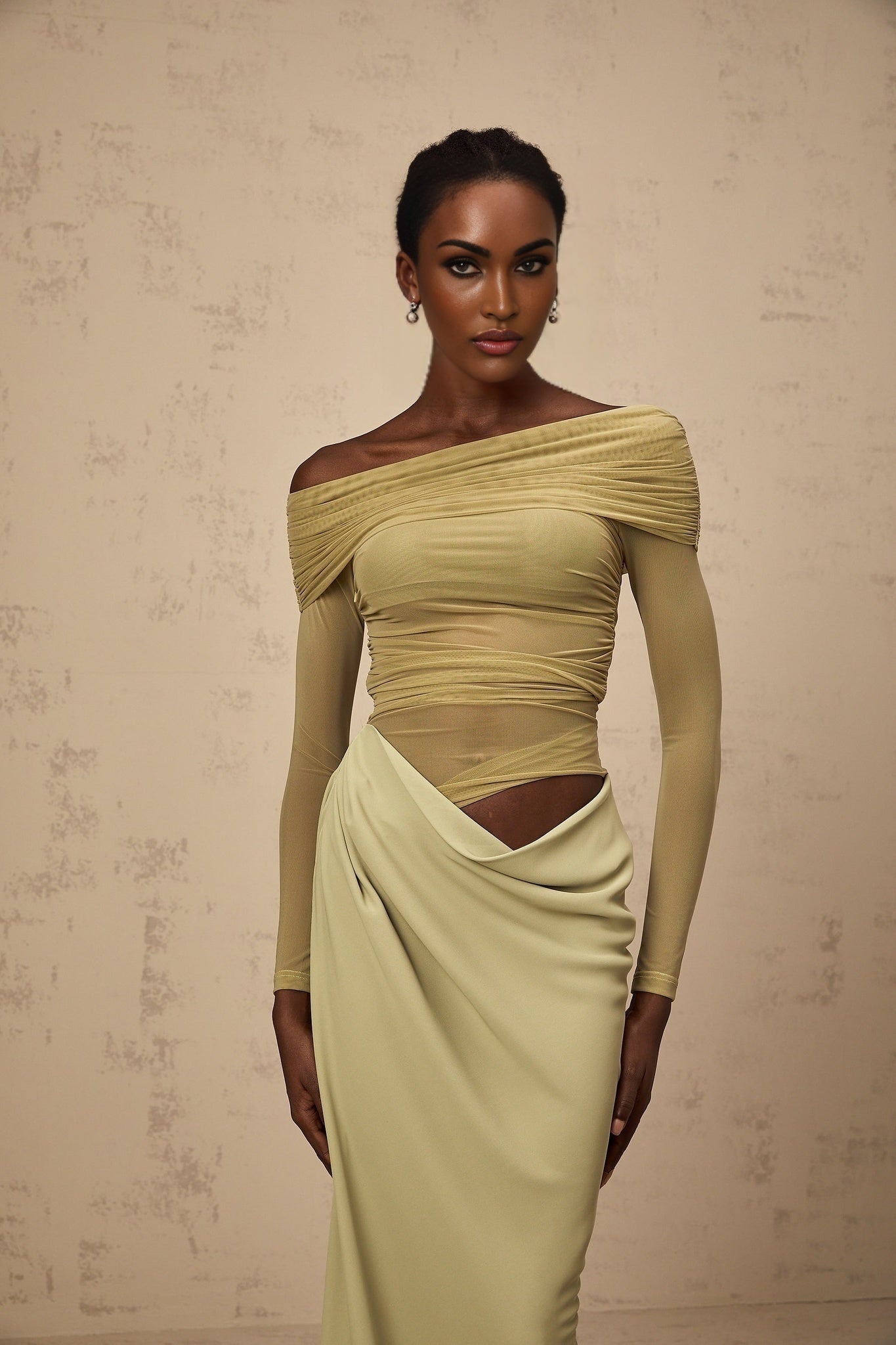 A green offshoulder midi dress with a semisheer fabric worn by a model standing in a neutral background