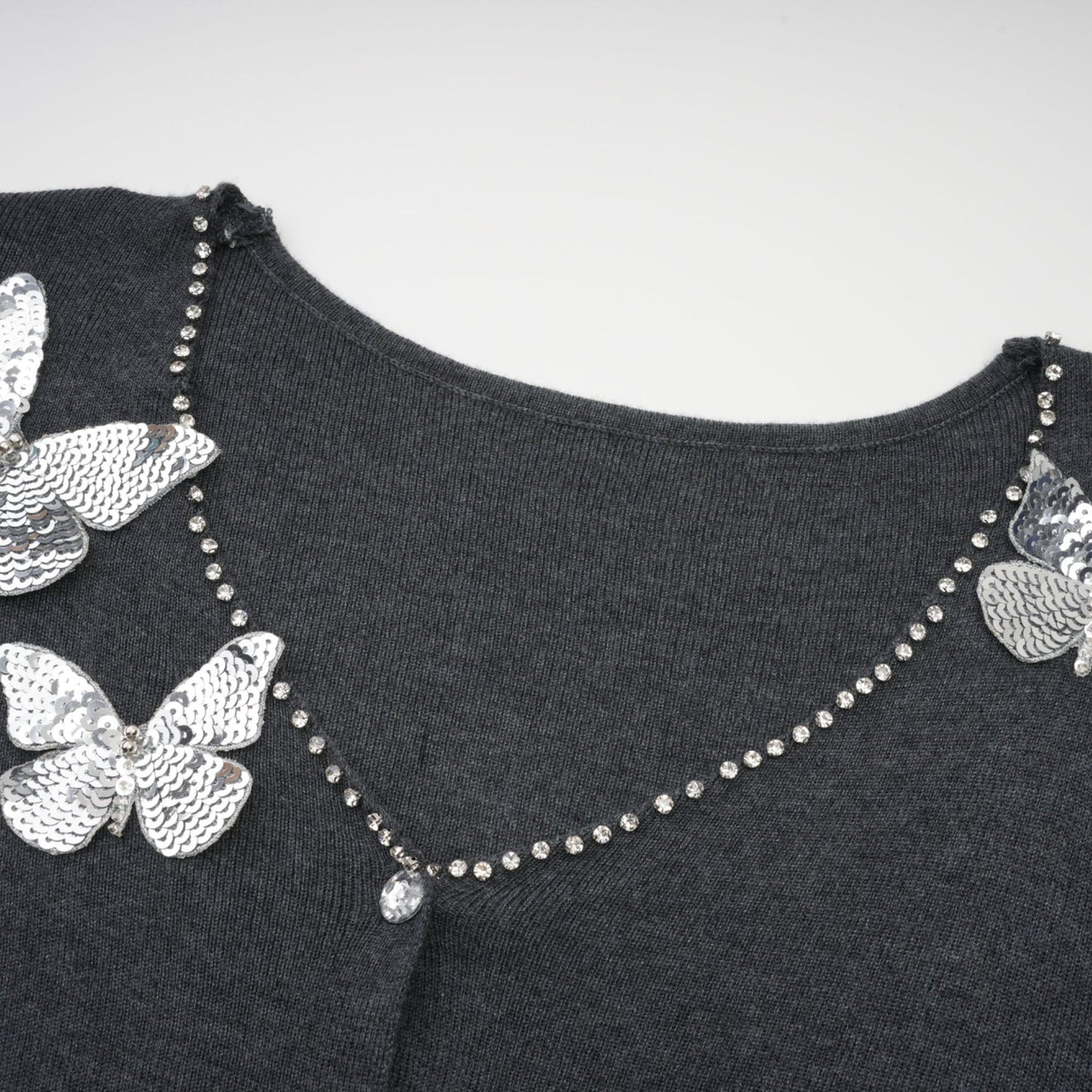 A grey cardigan with sequined butterfly designs scattered across the fabric creating a shimmering effect