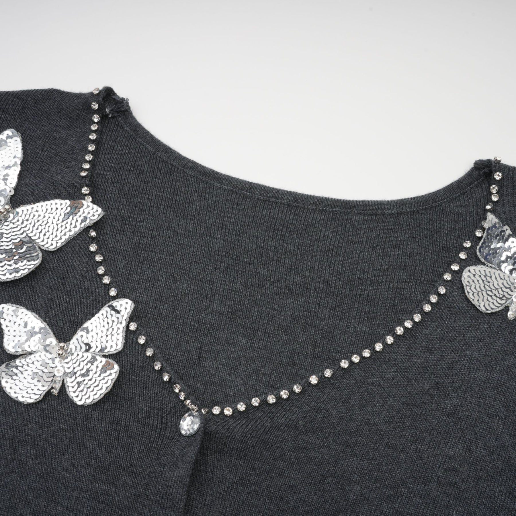 A grey cardigan with sequined butterfly designs scattered across the fabric creating a shimmering effect