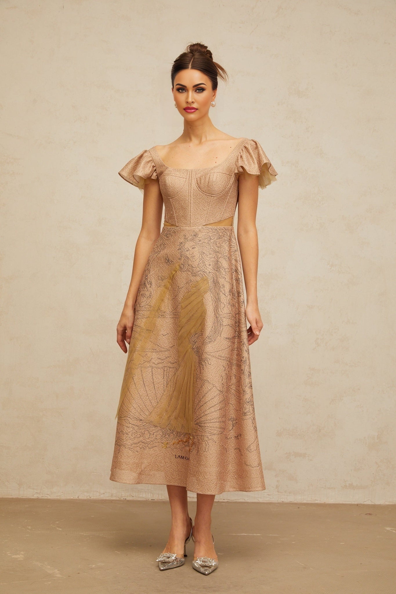 A khaki midi dress with a flared skirt featuring a graphic print pattern worn by a model standing in a neutral background