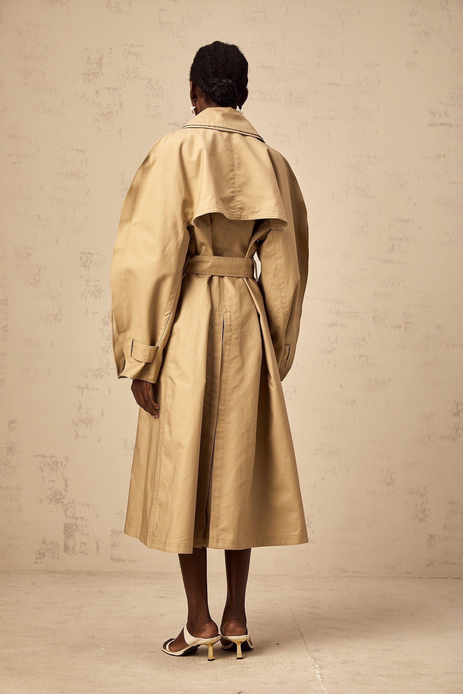 A khaki trench coat with curved sleeves modeled by someone named Jaden or in a style associated with Jaden