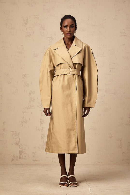 A khaki trench coat with curved sleeves worn by a model named Jaden standing against a plain background