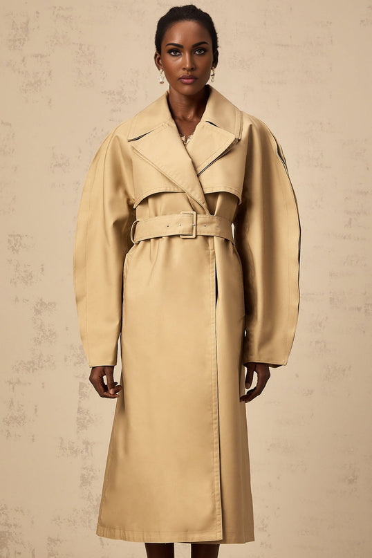 A khaki trench coat with curved sleeves worn by a model standing against a plain background