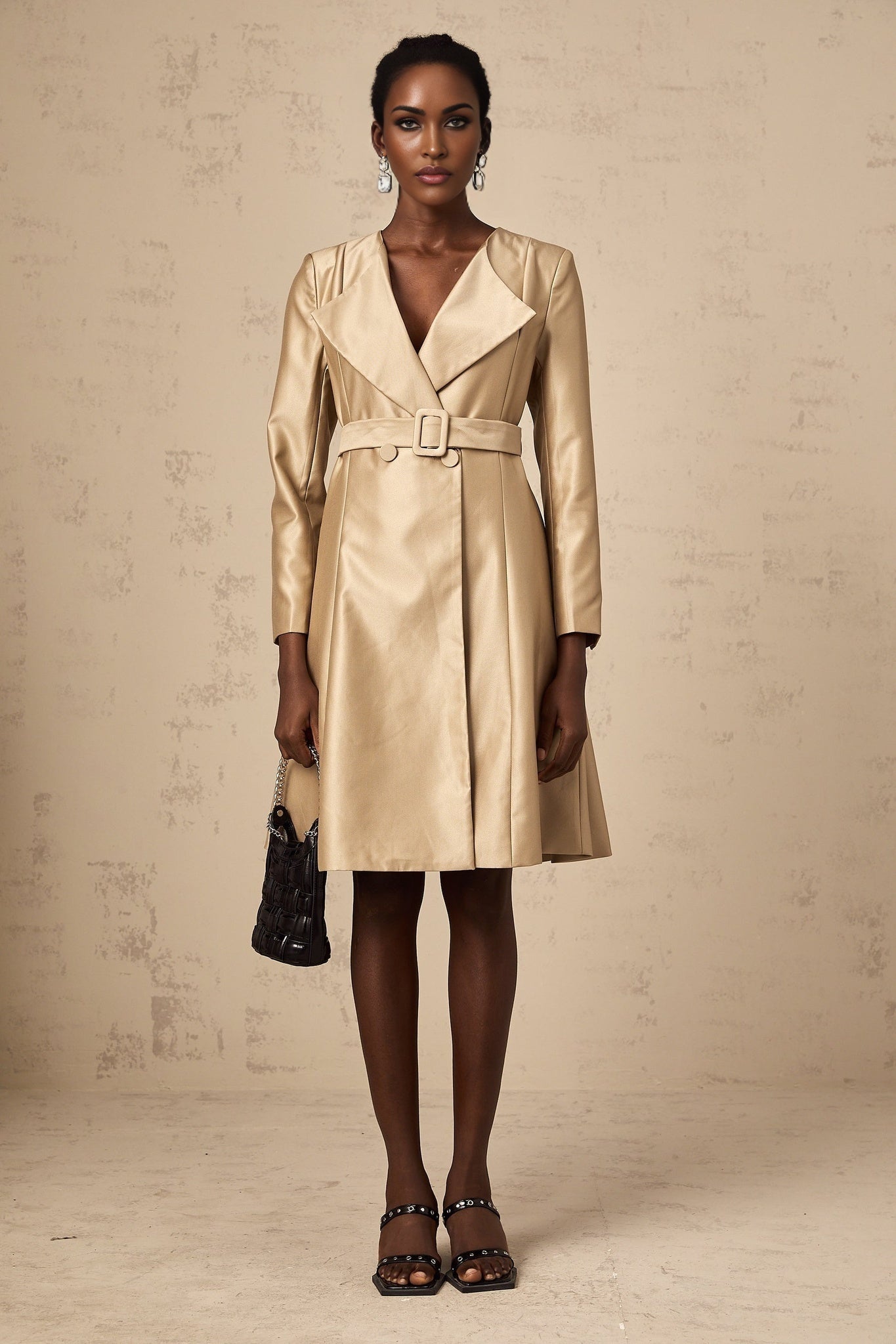 A khakicolored long coat with a belt at the waist named Roxane