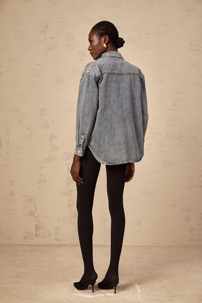 A light blue denim shirt with sparkling rhinestone embellishments on the front featuring a western style design and snap button closure
