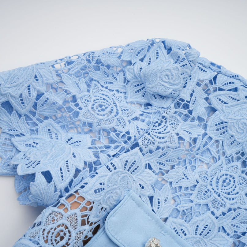 A light blue mini dress with ruffled lace detailing and floral applique designs featuring a fitted bodice and short skirt