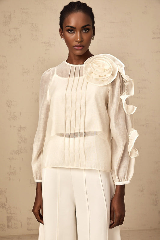 A light colored blouse with three dimensional floral details and a semi sheer fabric