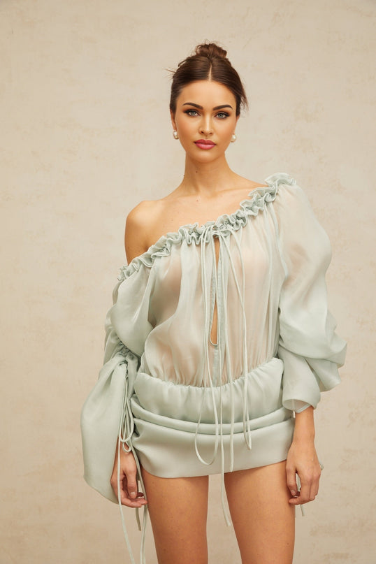 A light green mini dress with ruched fabric and ruffled trim details named Beryl