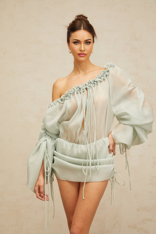 A light green mini dress with ruched fabric and ruffled trim details named Beryl