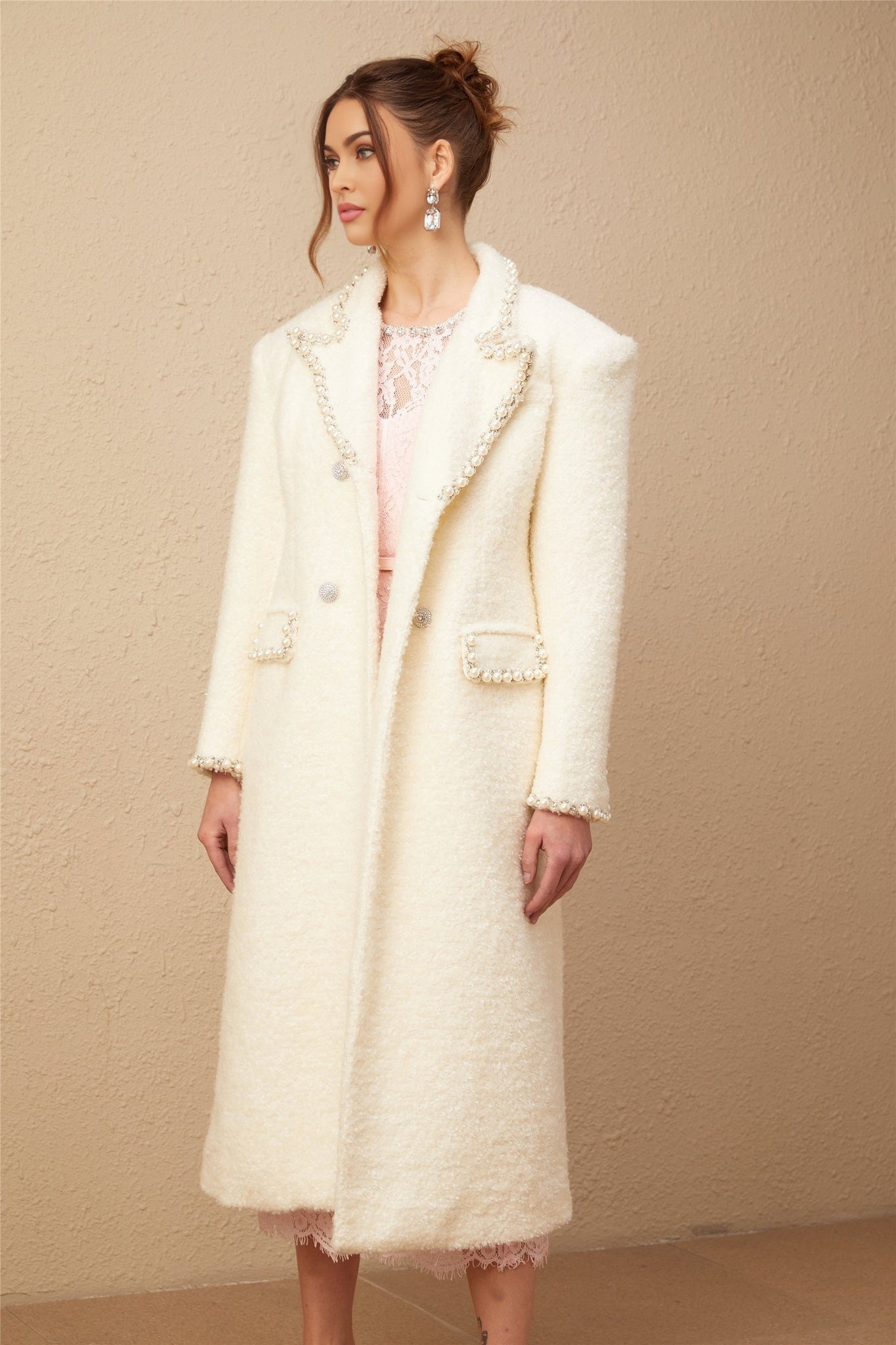 A long beige tweed coat with wool texture and faux pearl embellishments adorning the collar and pockets