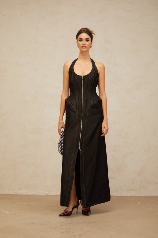 A long black denim maxi dress with a front slit and contrasting white stitching details worn by a model standing against a plain background
