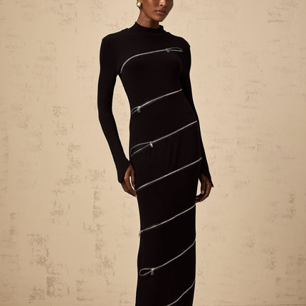 A long black fitted maxi dress with zipper details worn by a model standing against a plain background