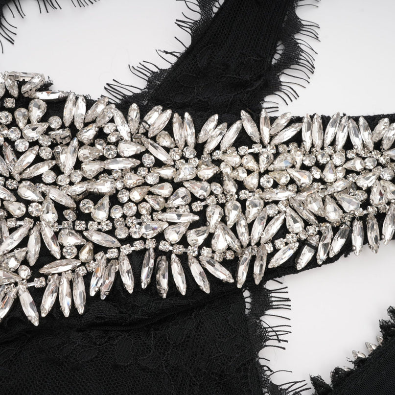 A long black maxi dress with a crossover neckline and crystal embellishments worn by a model standing against a plain background