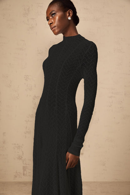 A long black maxi dress with a wavy lace pattern covering the entire garment called the Athena dress