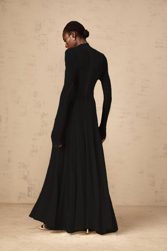 A long black maxi dress with a wavy lace pattern covering the entire garment The dress features a fitted bodice and flows into a fulllength skirt
