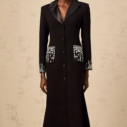 A long black maxi dress with blazer style top featuring embellishments worn by a model against a plain background