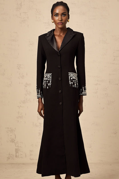 A long black maxi dress with blazer style top featuring embellishments worn by a model against a plain background