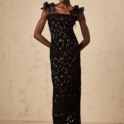 A long black maxi dress with colorful floral embroidery details worn by a model standing against a plain background