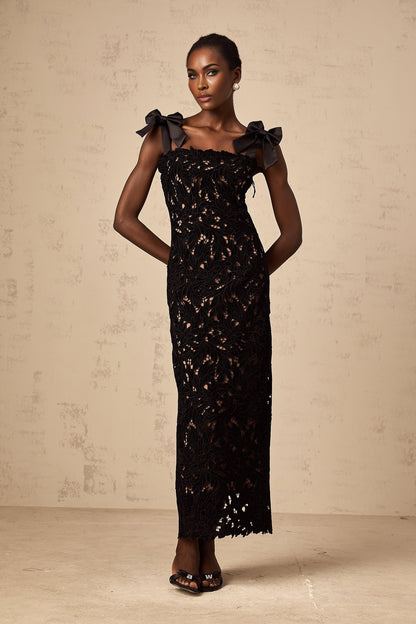 A long black maxi dress with colorful floral embroidery details worn by a model standing against a plain background