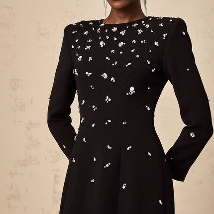 A long black maxi dress with crystal embellishments on the fabric sparkling against the dark background