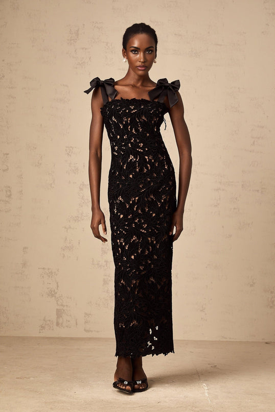 A long black maxi dress with delicate floral embroidery details worn by a model standing against a plain background