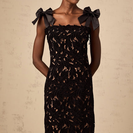 A long black maxi dress with delicate floral embroidery details worn by a woman standing against a plain background