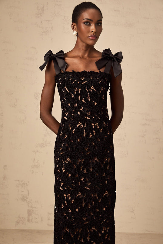 A long black maxi dress with delicate floral embroidery details worn by a woman standing against a plain background