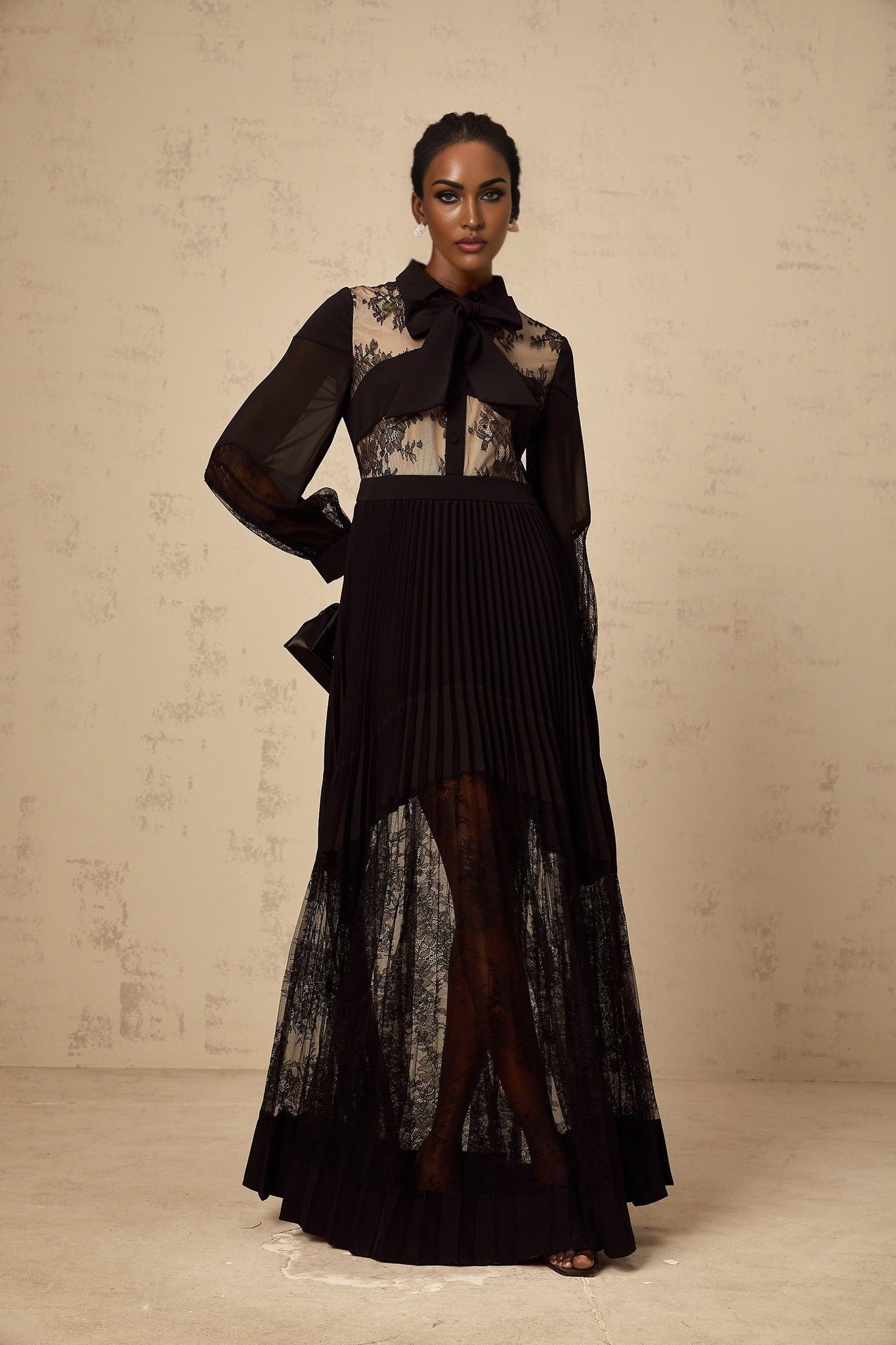 A long black maxi dress with pleated skirt and floral lace panels featuring a fitted bodice and flowing silhouette