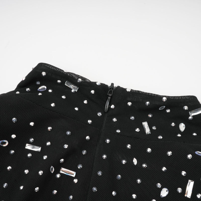 A long black semi sheer maxi dress with embellished details worn by a model standing against a plain background