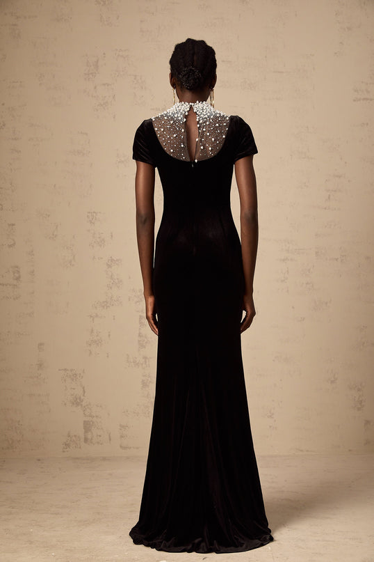 A long black velvet maxi dress with faux pearl embellishments worn by a model against a plain background